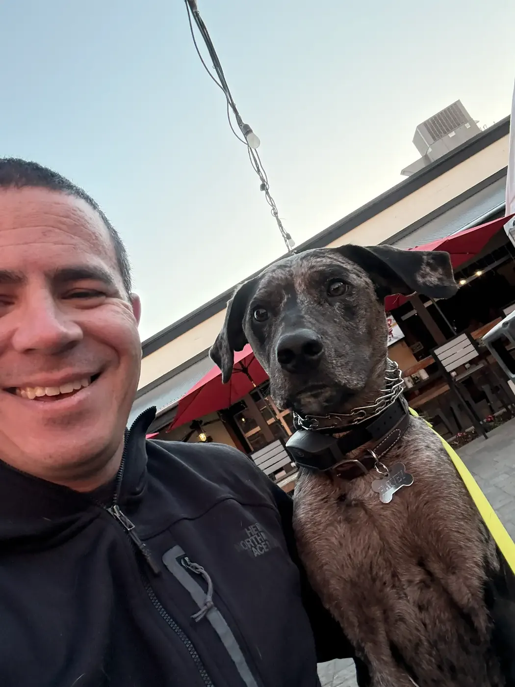 Derek Weaver smiling beside a brindle dog wearing a training collar on a downtown walk